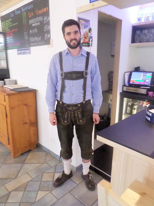 Thibaud Euler en tenue traditionnelle de brasseur bavarois (lederhose et chemise à carreaux bleus) devant le comptoir d'Au Bavarois.
